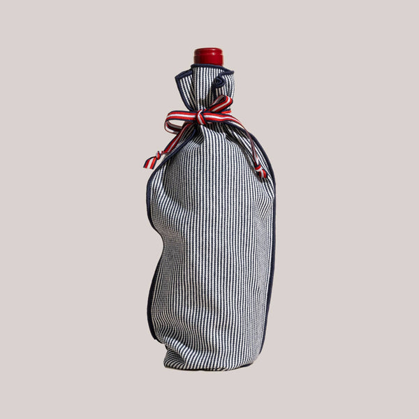 Bottle wrapped in a blue and white striped fabric with a red ribbon on a beige background