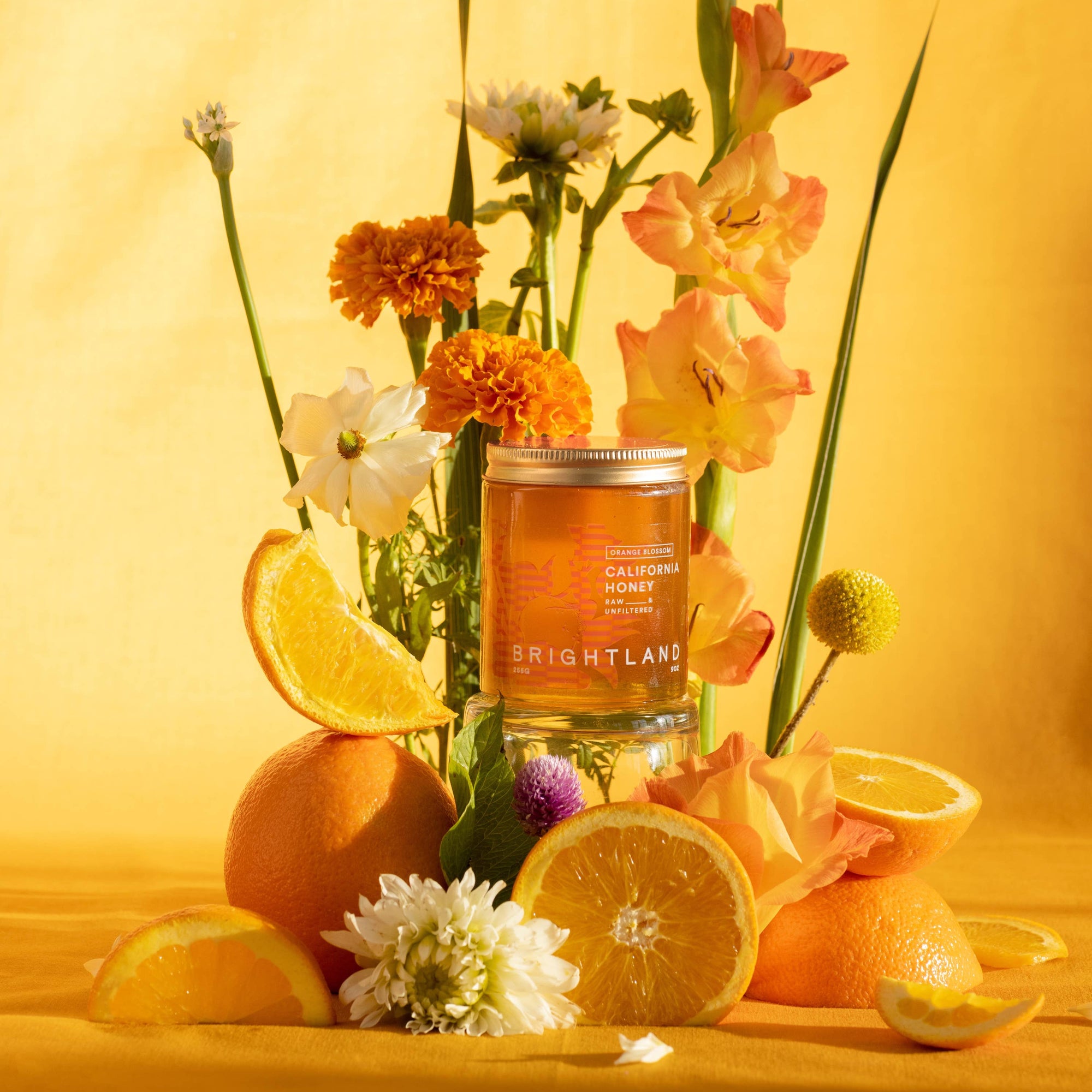 Candle in a glass jar surrounded by lemons, oranges, and flowers on a yellow background
