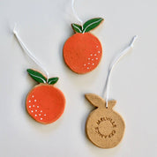 Three handmade ceramic orange ornaments with green stems, each with white hanging tags.