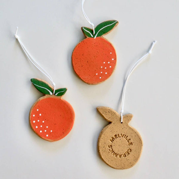 Three handmade ceramic orange ornaments with green stems, each with white hanging tags.