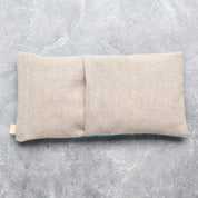 A rectangular beige linen eye mask pillow with a central fold, shown on a textured gray concrete surface.