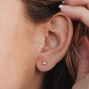 Close-up of an ear with a small stud earring, hair being adjusted.