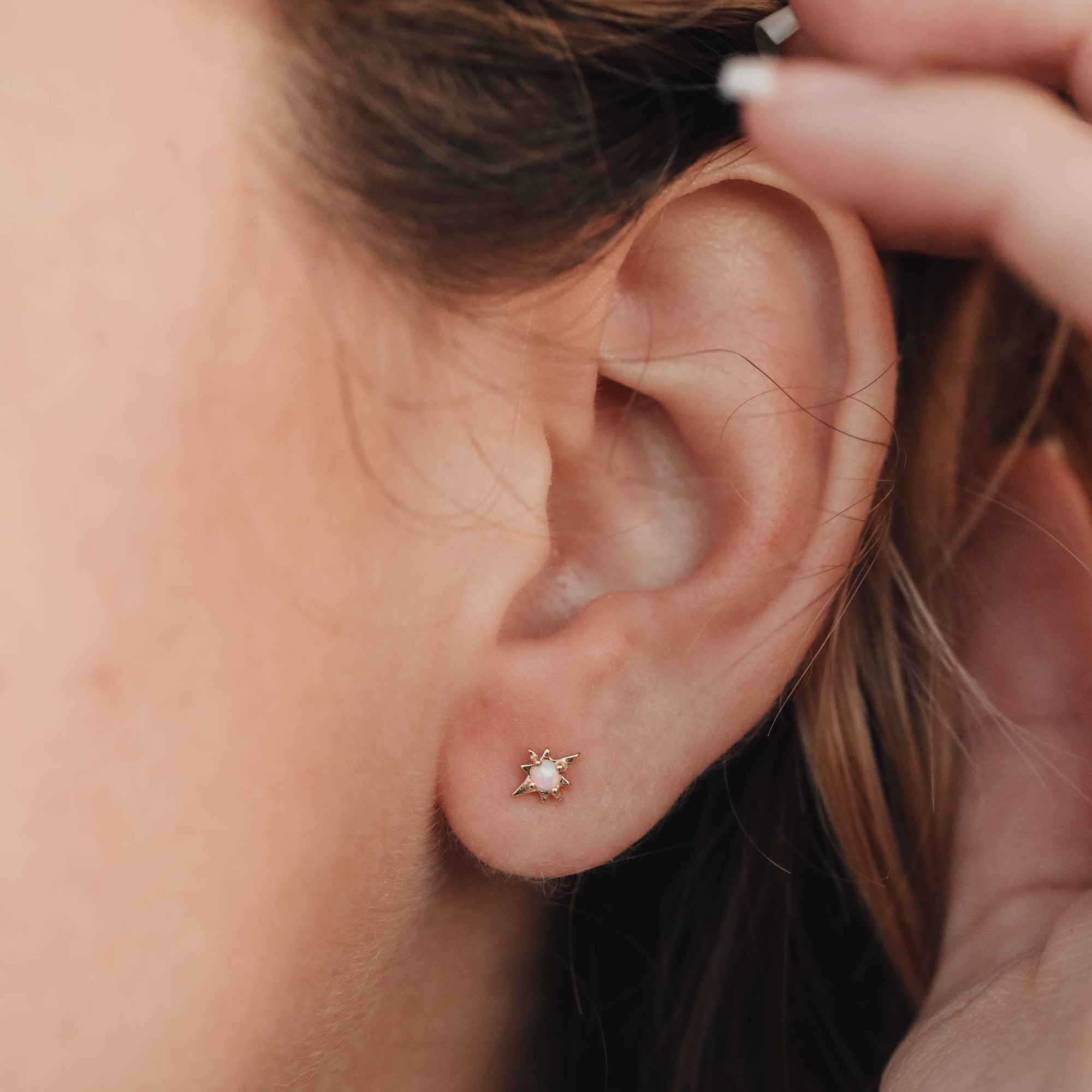 Close-up of an ear with a small stud earring, hair being adjusted.