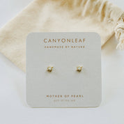 Pair of gold earrings on a Canyonleaf branded card with a beige drawstring bag in the background.