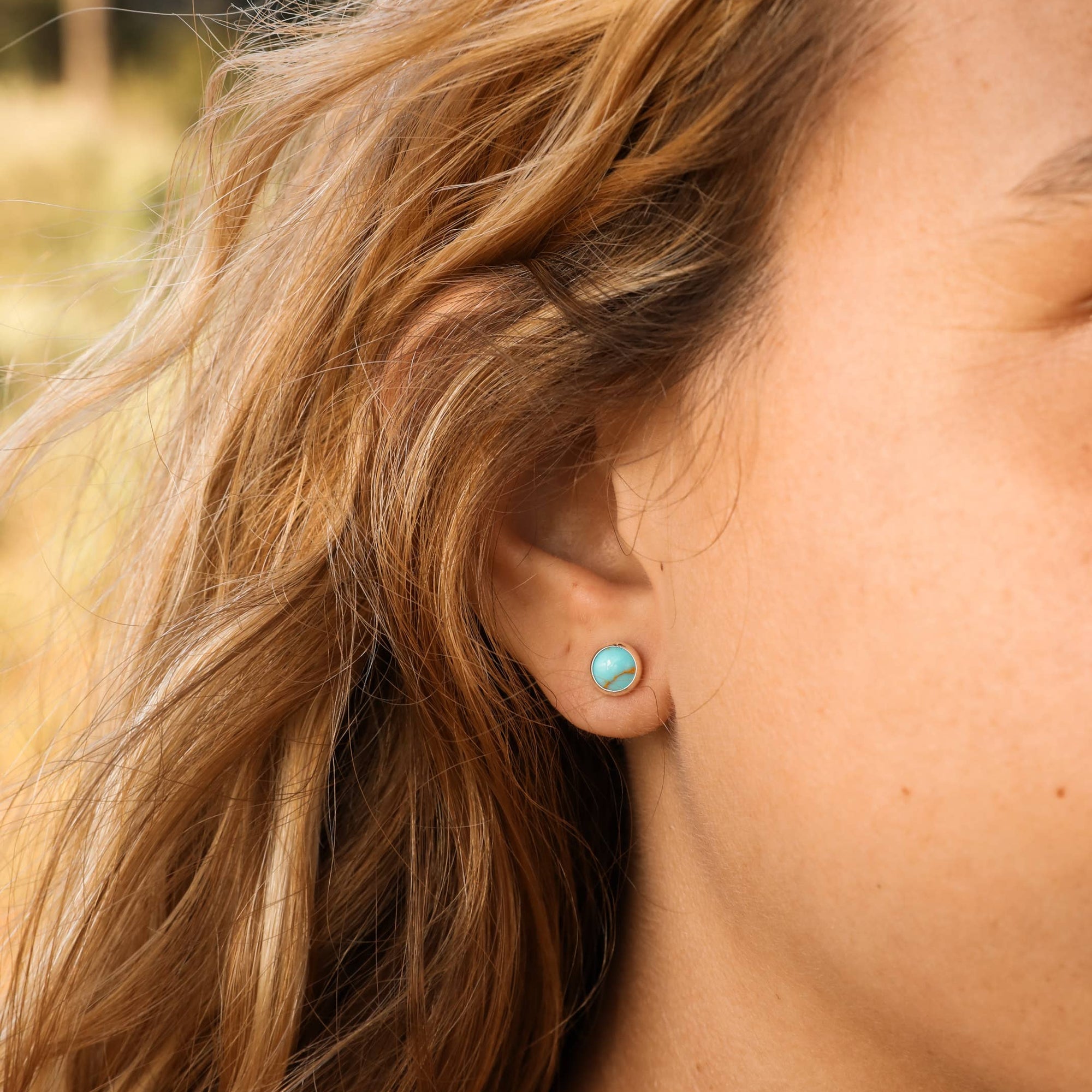 Close-up of a person wearing turquoise earrings with a blurred natural background