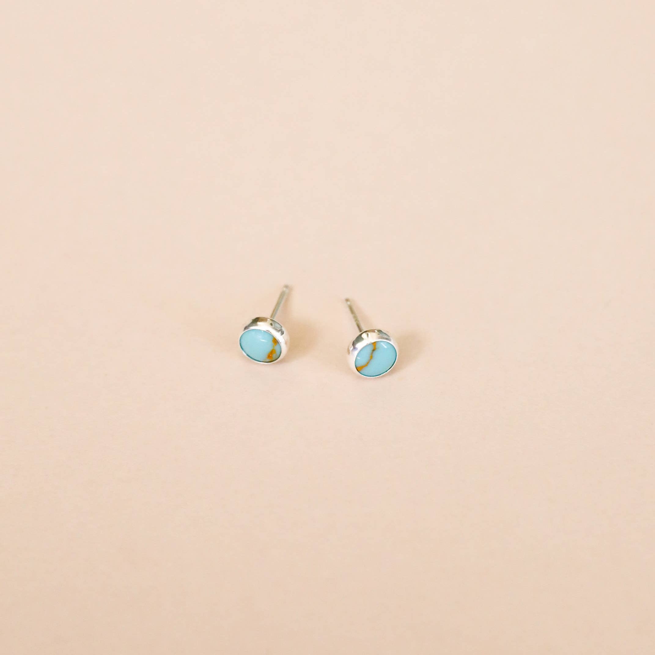 Pair of silver earrings with turquoise stones on a beige background