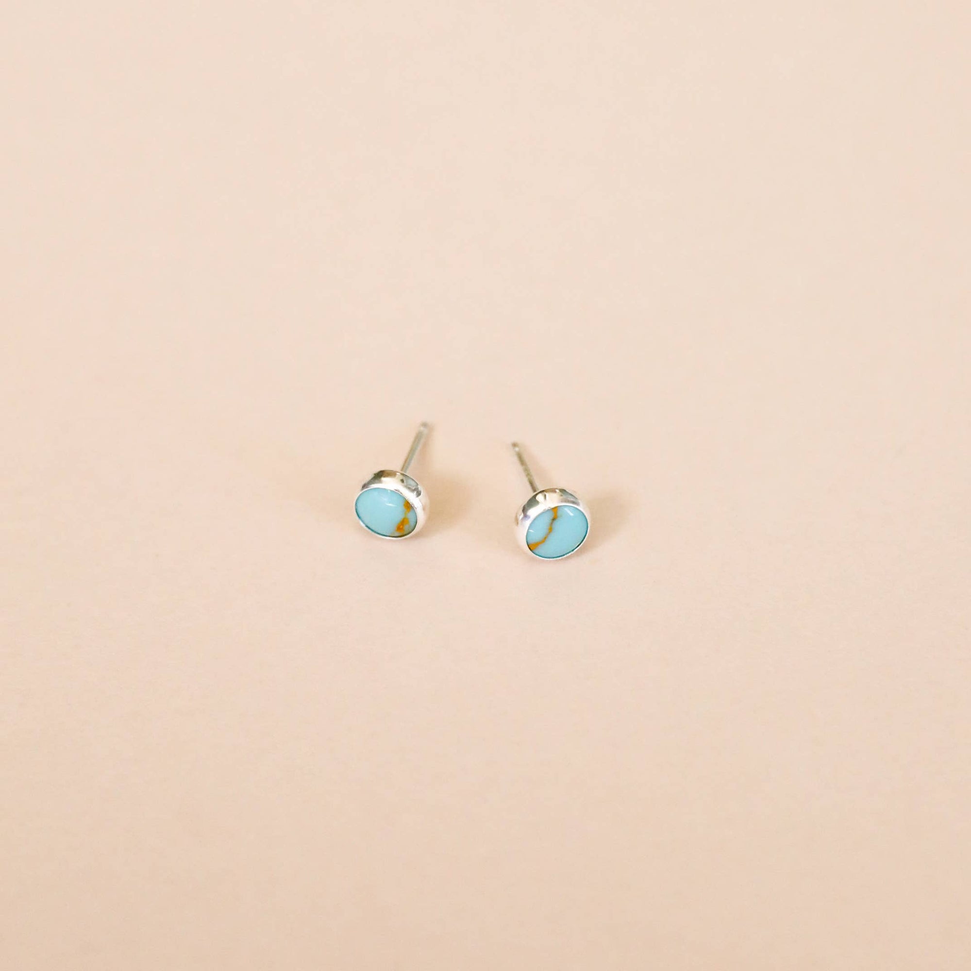 Pair of silver earrings with turquoise stones on a beige background