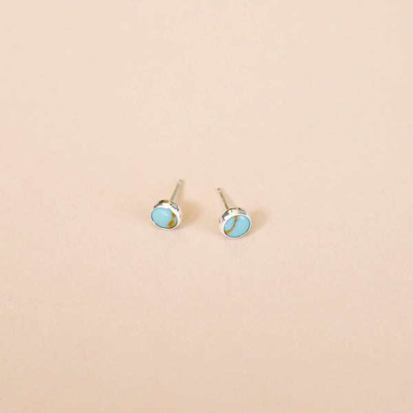Pair of silver earrings with turquoise stones on a beige background