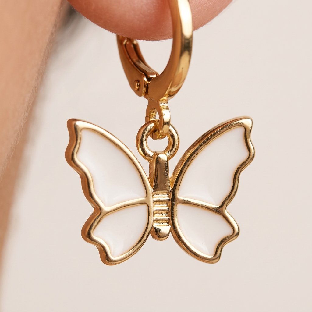 Gold butterfly earring held by a hand against a neutral background