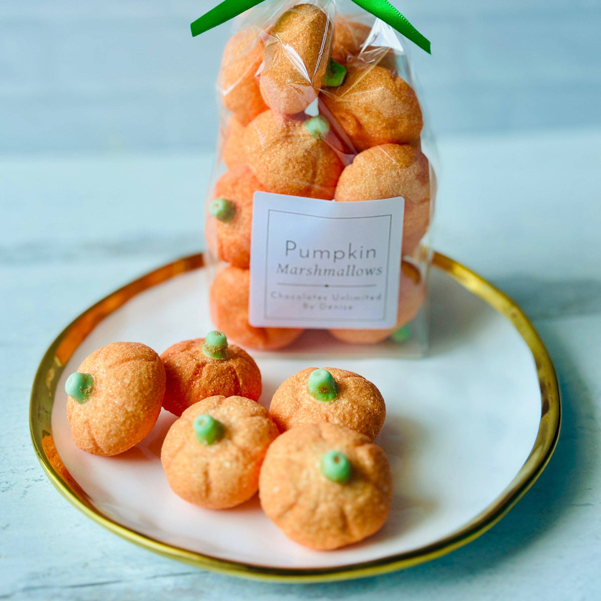 A ceramic plate on a wooden table with a small group of pumpkin shaped marshmallows at the forefront.