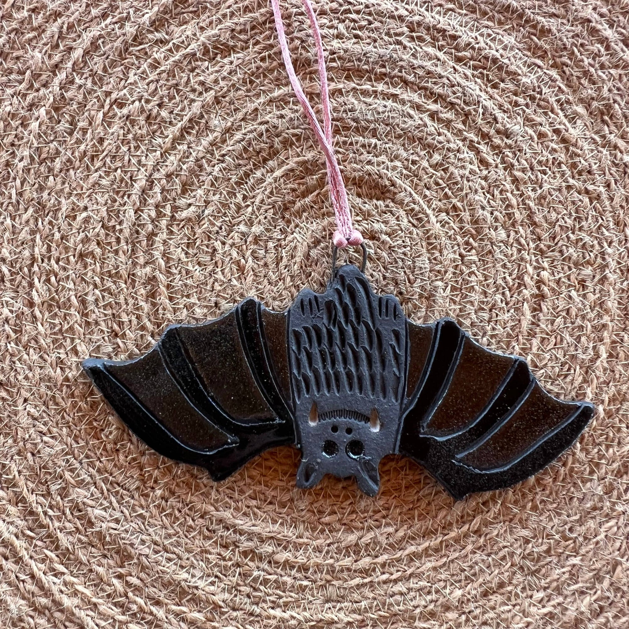 Black bat-shaped ornament on a pink string against a textured brown background