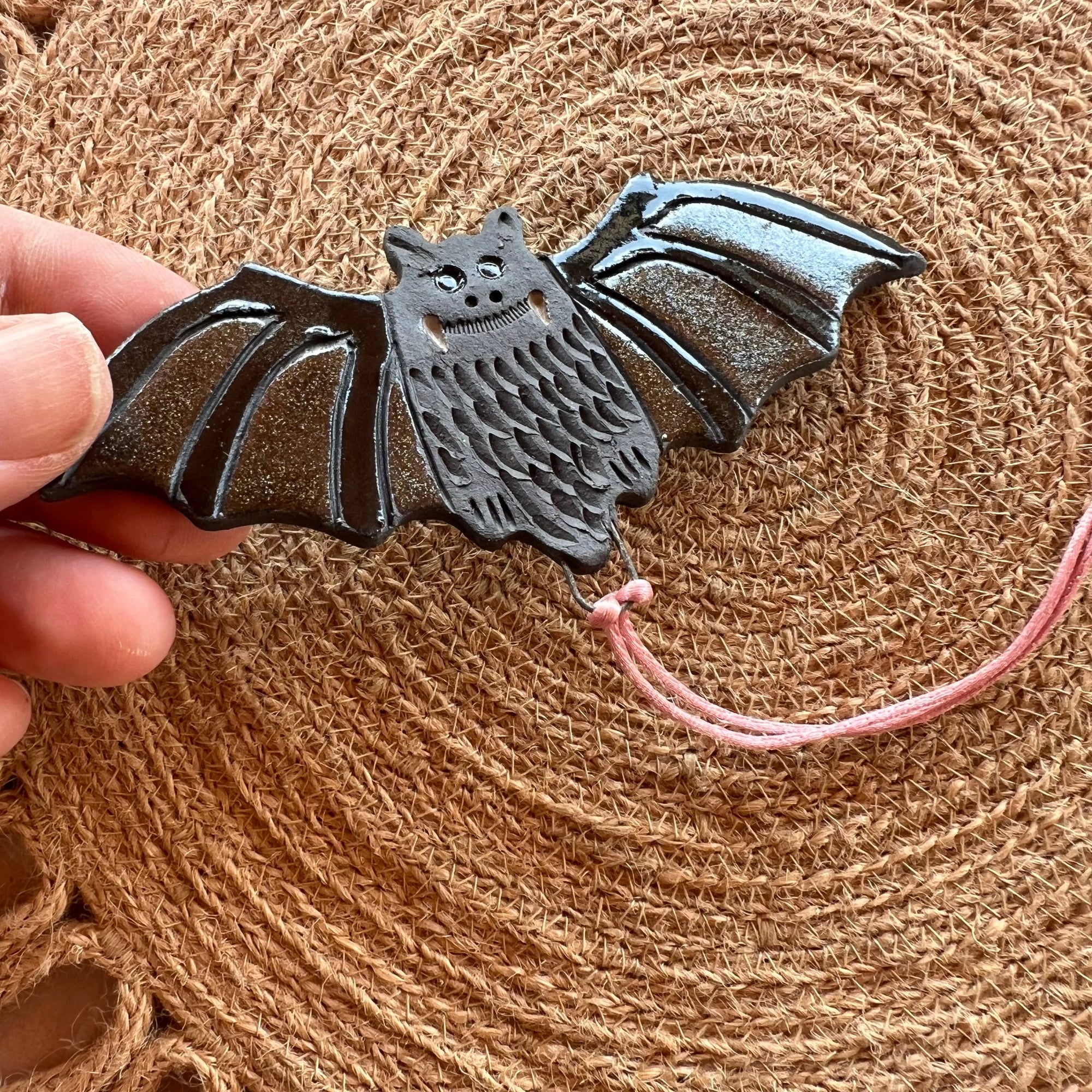 Ceramic bat-shaped ornament held by a hand on a textured brown background