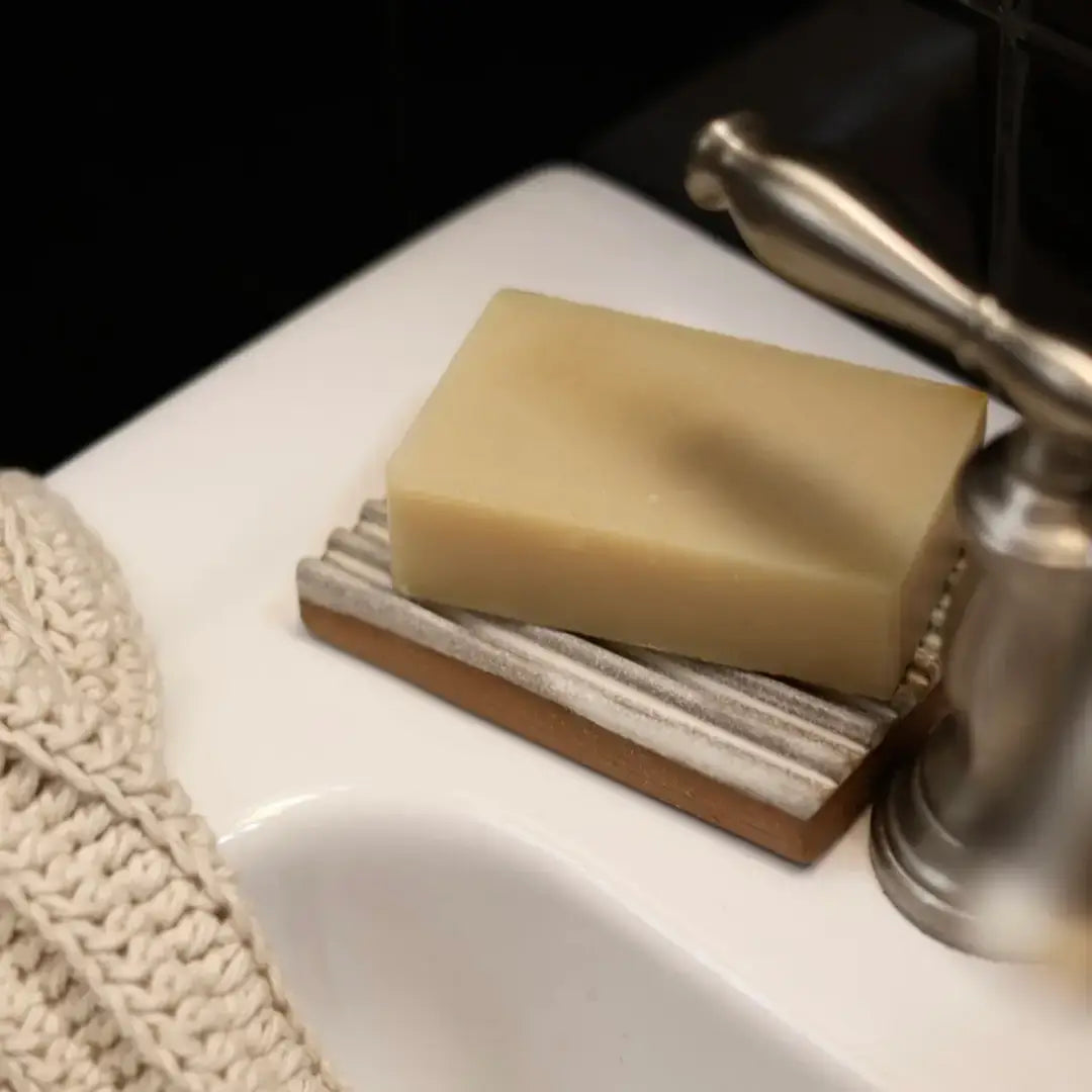 Bar of soap on a ceramic soap dish with a faucet in the background