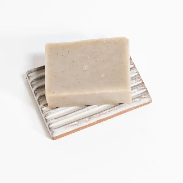 Bar of soap on an off-white ceramic soap dish against a white background