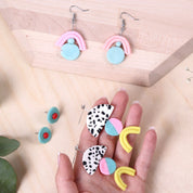 A hand holding a pair of ceramic earrings against a natural wood background.