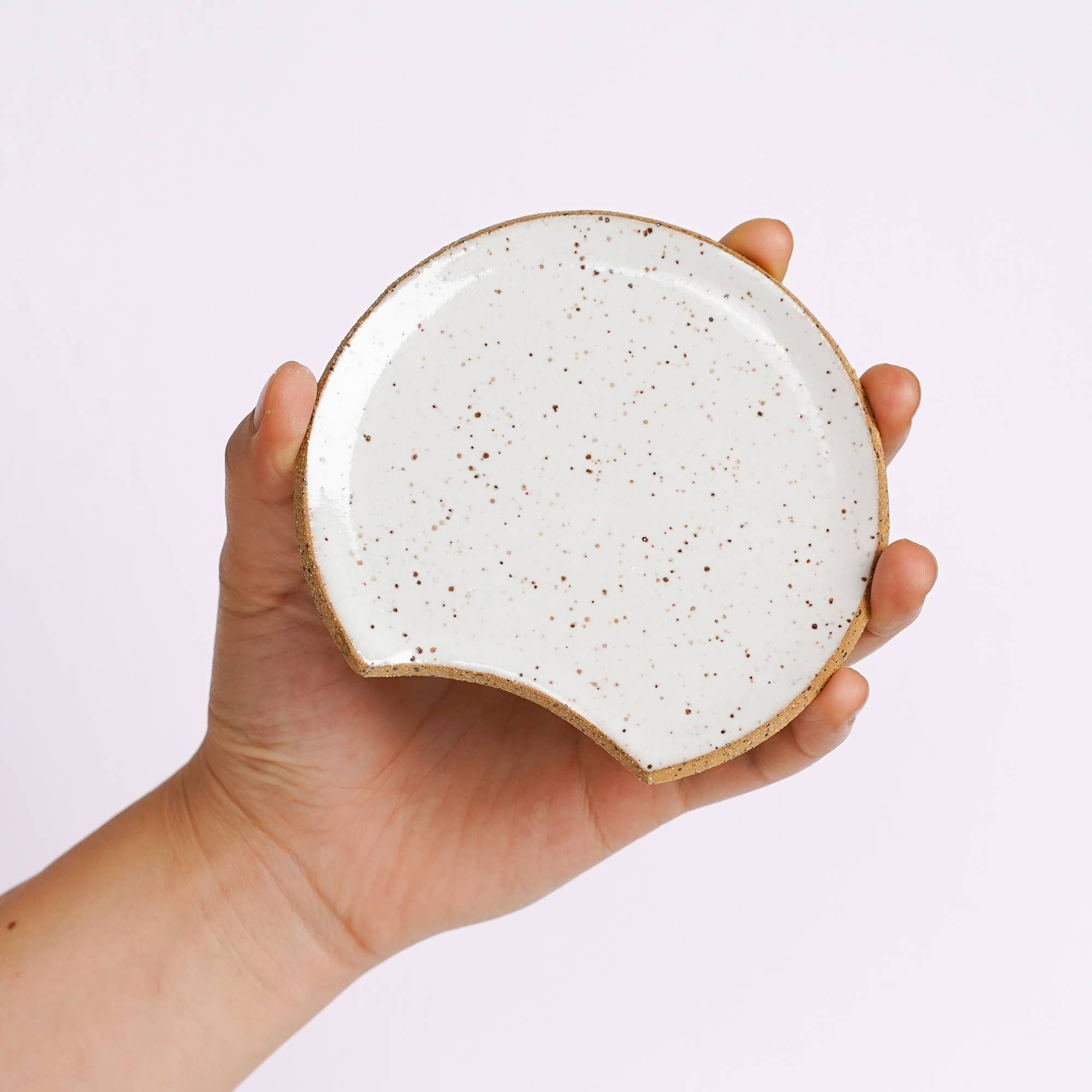 Hand holding a small speckled ceramic plate against a light purple background