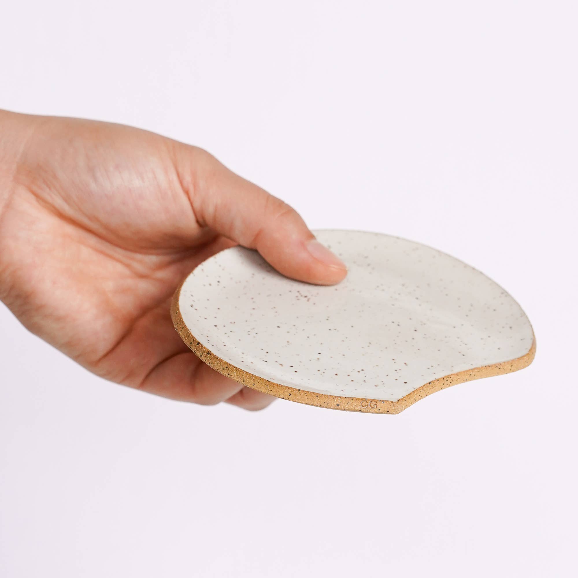 Hand holding a ceramic coaster with a speckled design on a light purple background