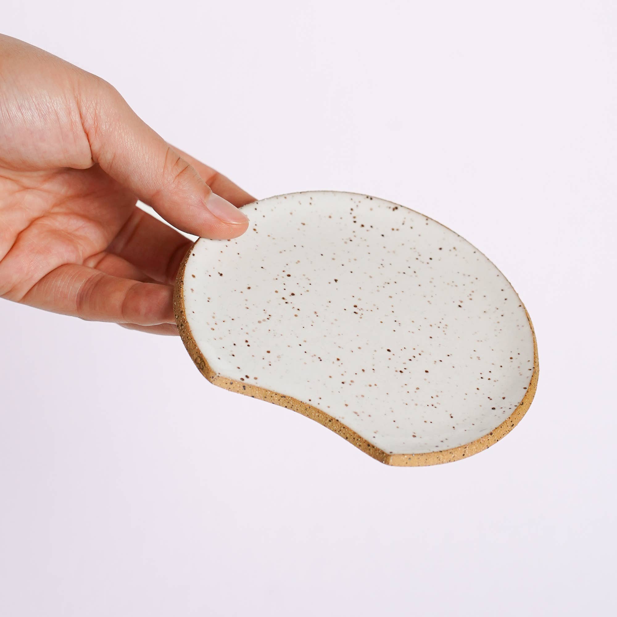 Hand holding a ceramic coaster with a speckled design on a light purple background