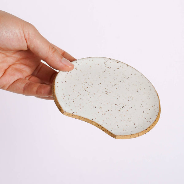 Hand holding a ceramic coaster with a speckled design on a light purple background