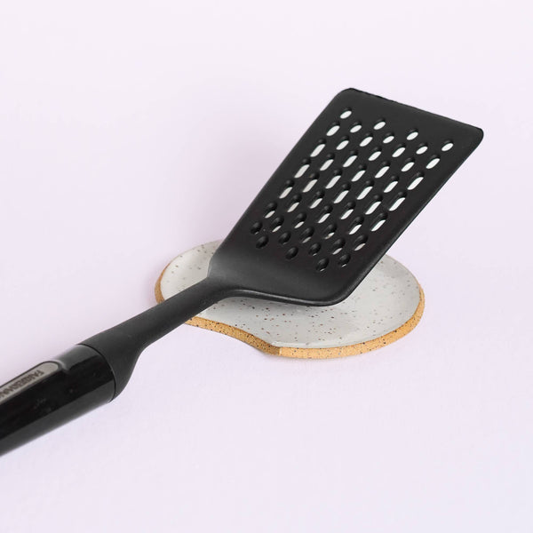 A spatula resting on a ceramic spoon rest on a plain background.