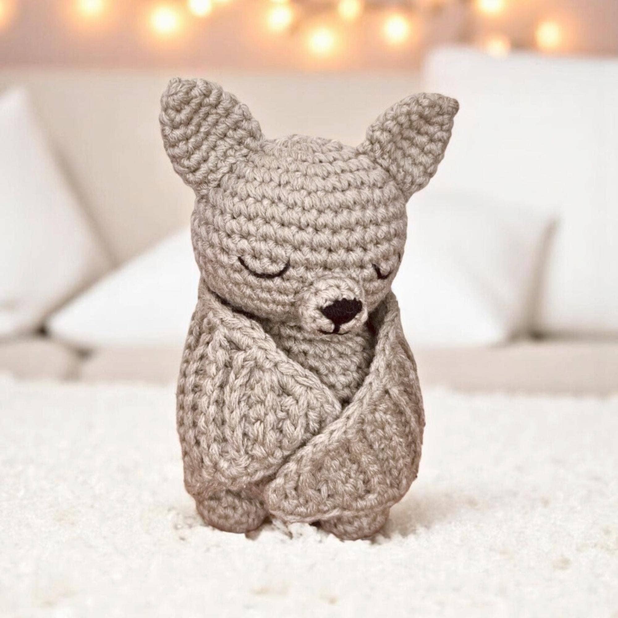 Crochet bat toy on a soft surface with blurred lights in the background