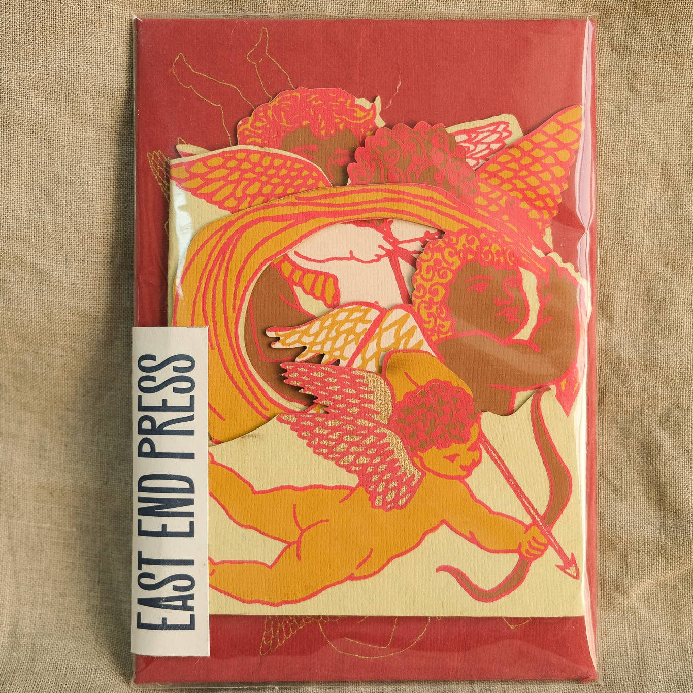 Folded card with cupid design on red background, placed on a textured surface.