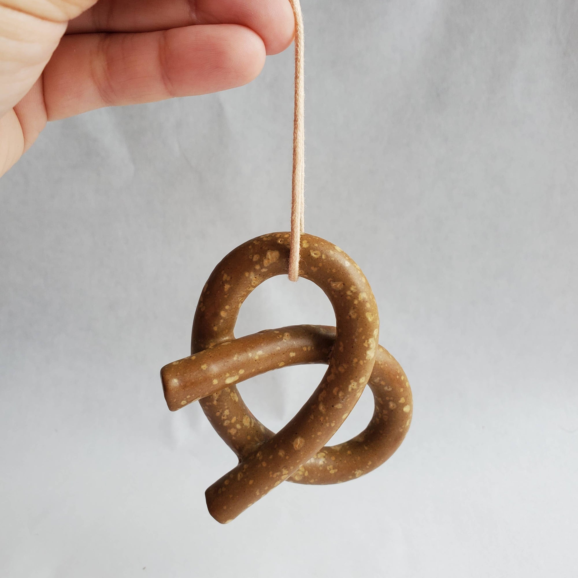 Hand holding a pretzel-shaped ornament on a string against a plain background