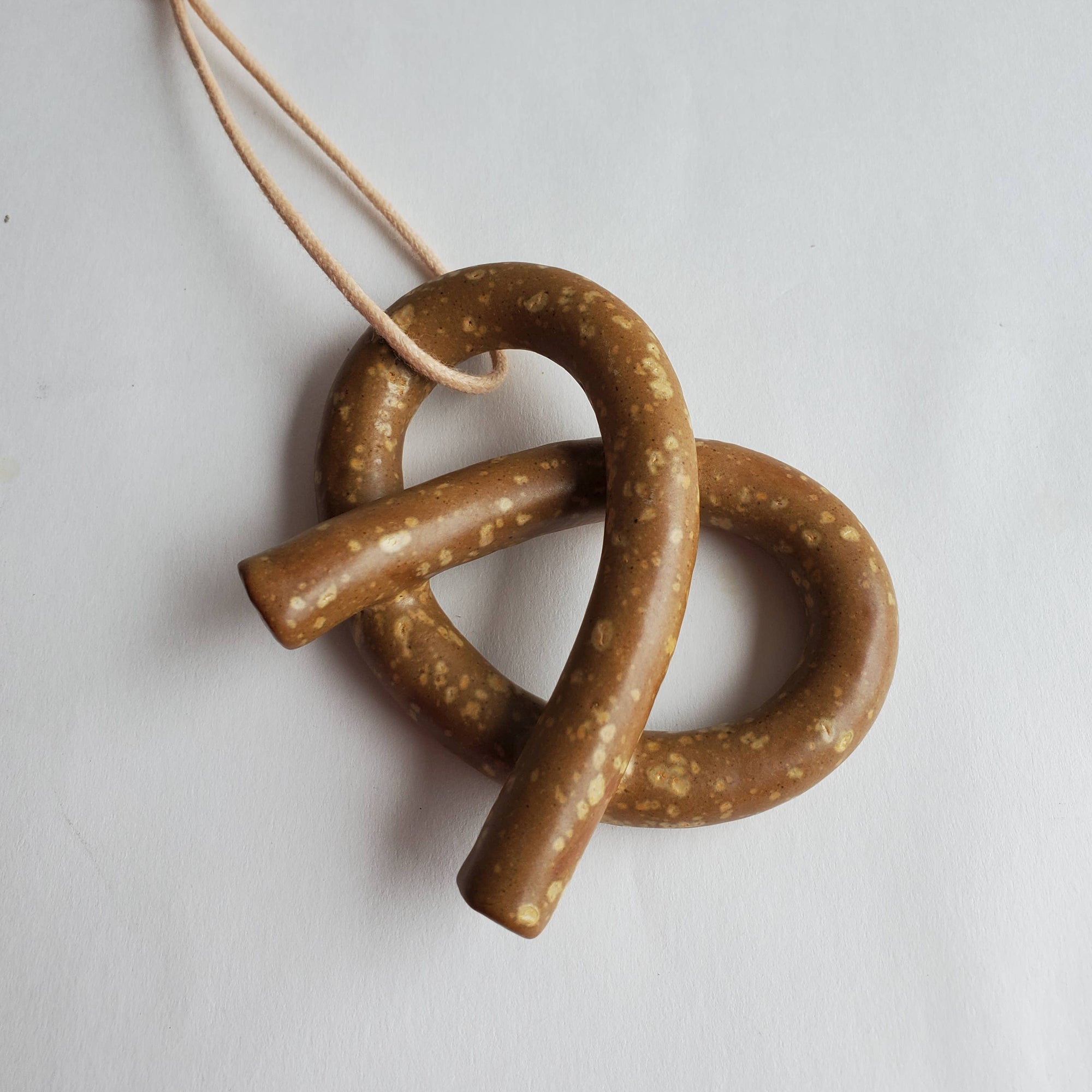 Brown ceramic pretzel ornament on a white background