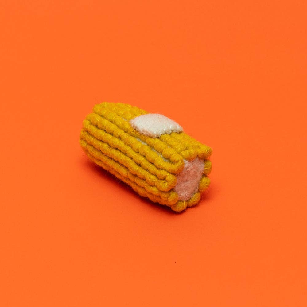 Corn on the cob dog toy with pat of butter on an orange background.