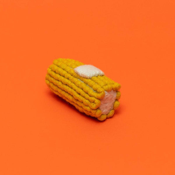 Corn on the cob dog toy with pat of butter on an orange background.