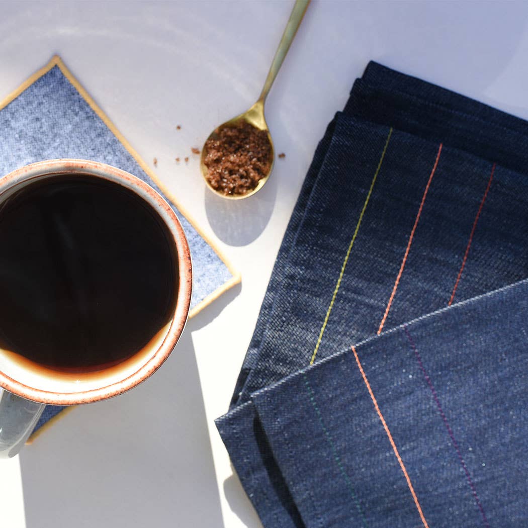 Cup of coffee with a spoonful of coffee grounds and denim fabric on a white surface