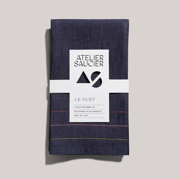 Two navy blue denim tea towels with a white label on a light gray background