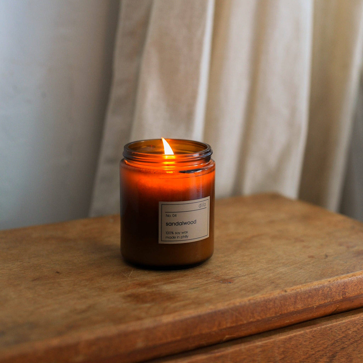 Candle in an amber jar with a label on a wooden surface and light background
