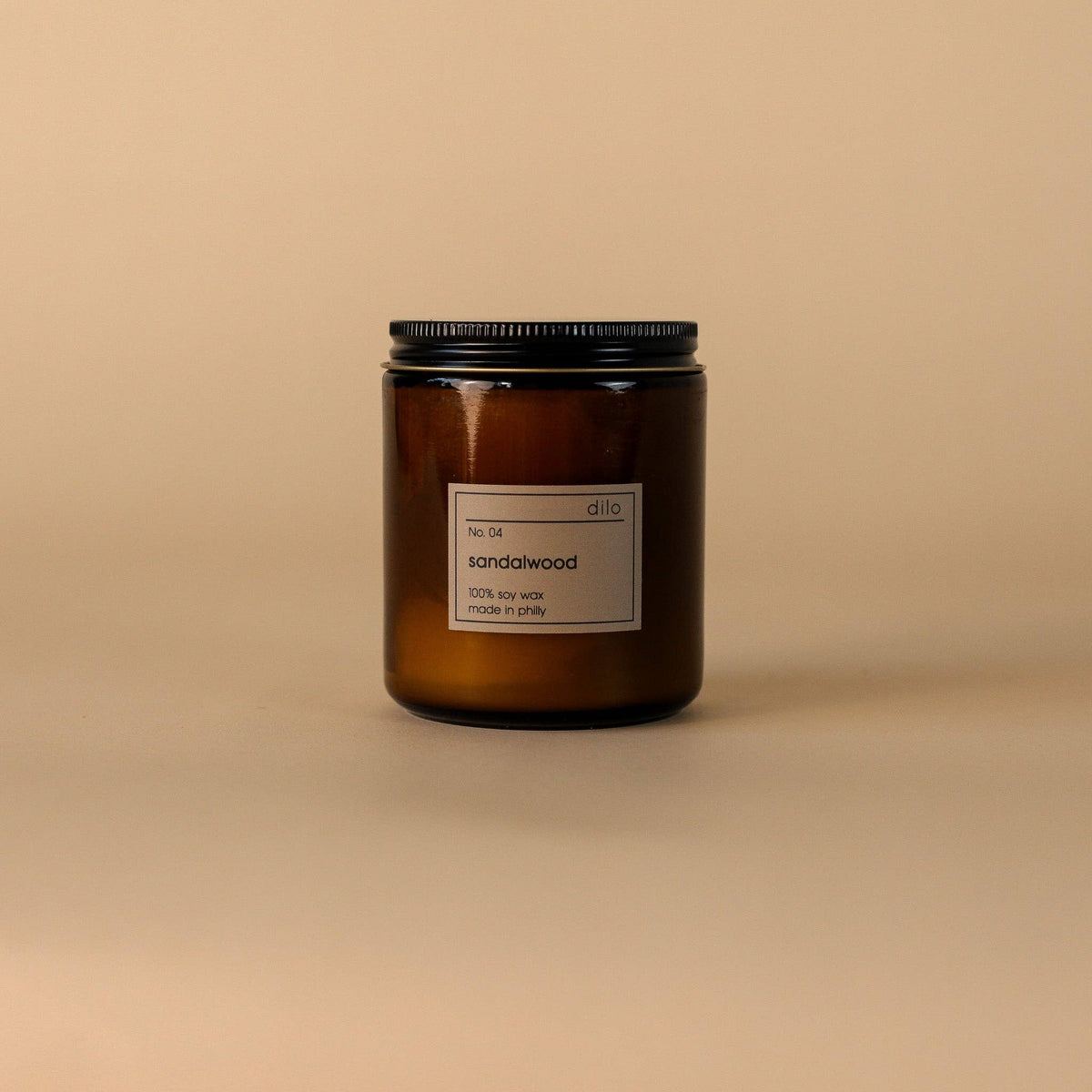 An amber glass jar candle with a black metal lid and a minimalist white label reading 'd10 sandalwood', set against a solid beige background.
