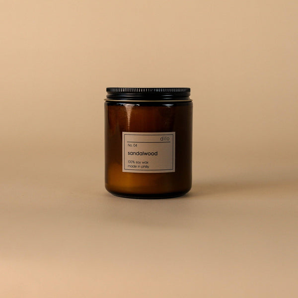 An amber glass jar candle with a black metal lid and a minimalist white label reading 'd10 sandalwood', set against a solid beige background.