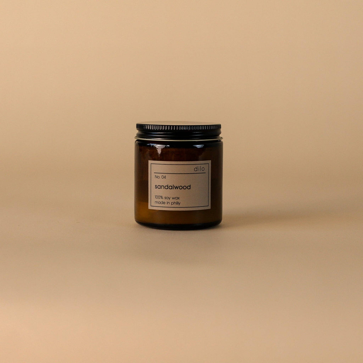 Sandalwood candle in a glass jar with a black lid on a beige background