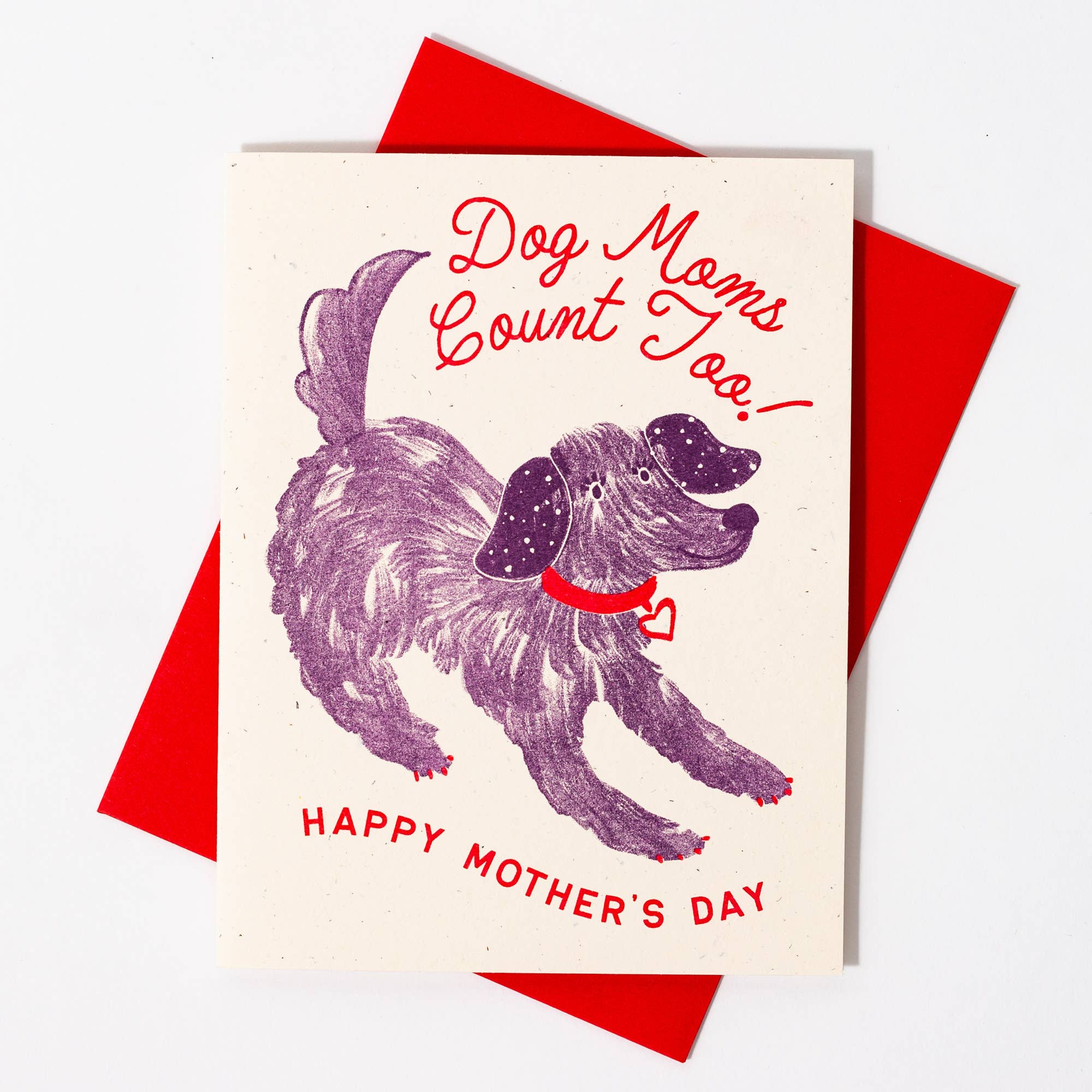 A greeting card with an illustration of a dog and the text 'Dog Moms Count Too! HAPPY MOTHER'S DAY' printed above. The card is shown with a red envelope.