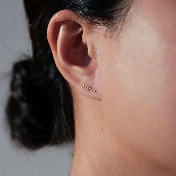 Close-up of an ear with a thin gold earring against a neutral background