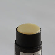 A close-up of a black cosmetic stick container with a pale yellow cream or balm product visible at the top, set against a plain light gray background.