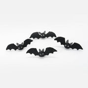 Five small black bat-shaped decorative figures with white eyes and gray ears, arranged on a plain light background.
