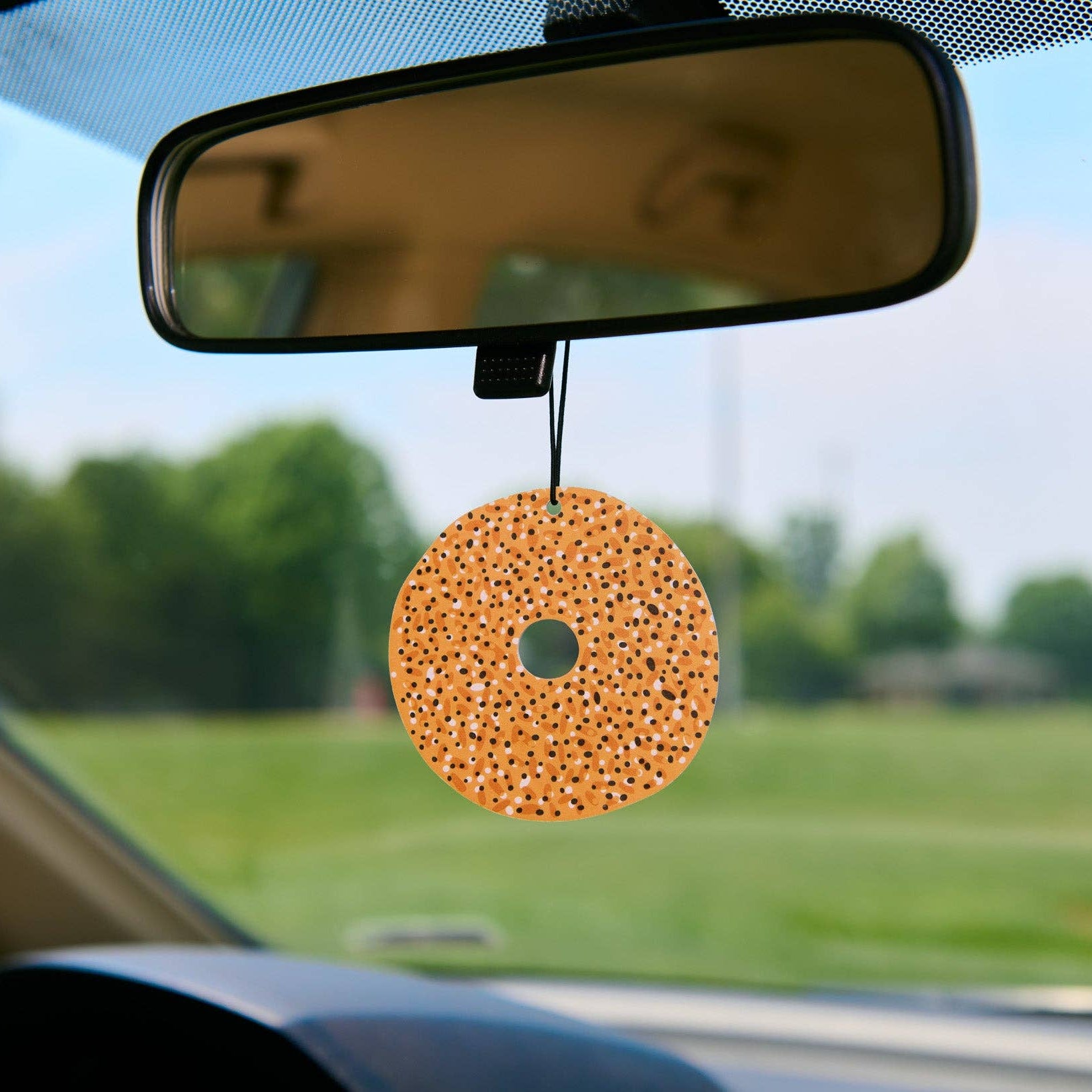 Bagel car air freshener hanging from a rearview mirror with a scenic background