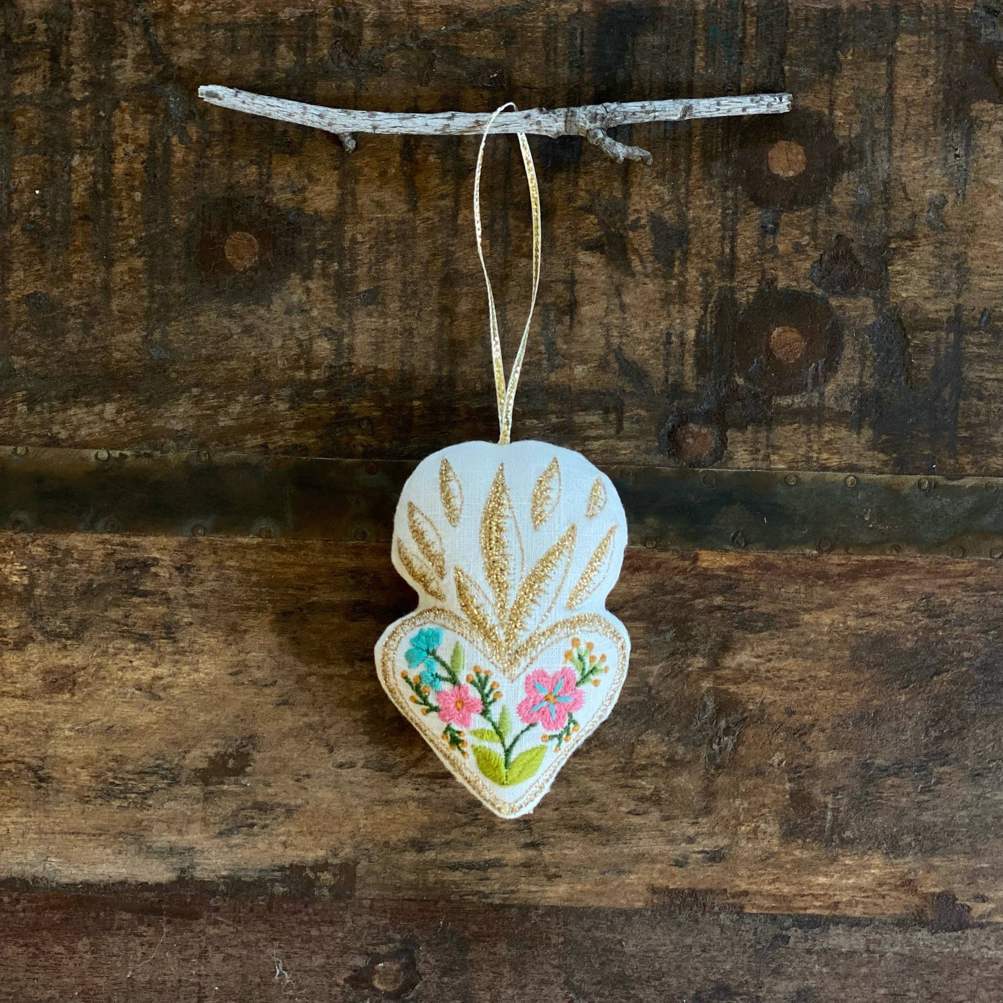 Decorative heart-shaped ornament with floral design hanging on a wooden branch.