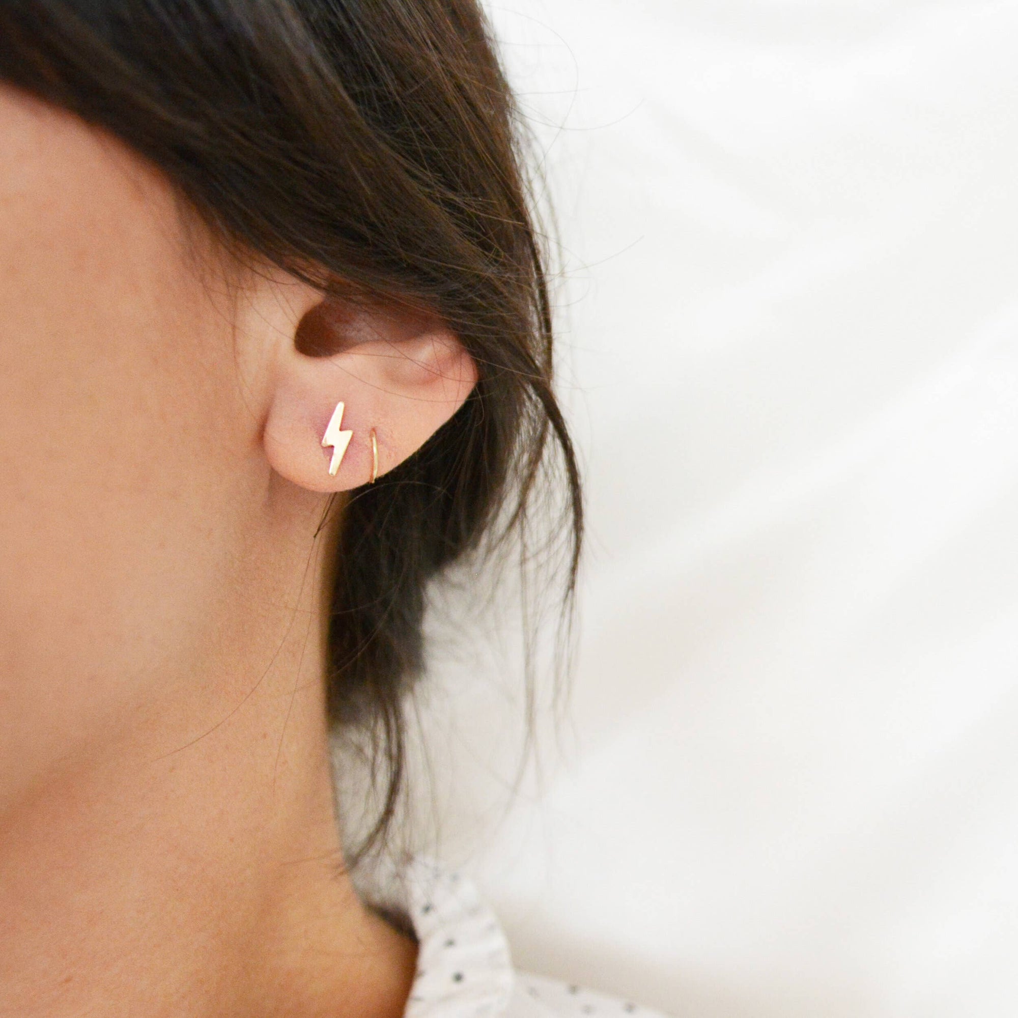 Gold lightning bolt earring worn by a person on a blurred background