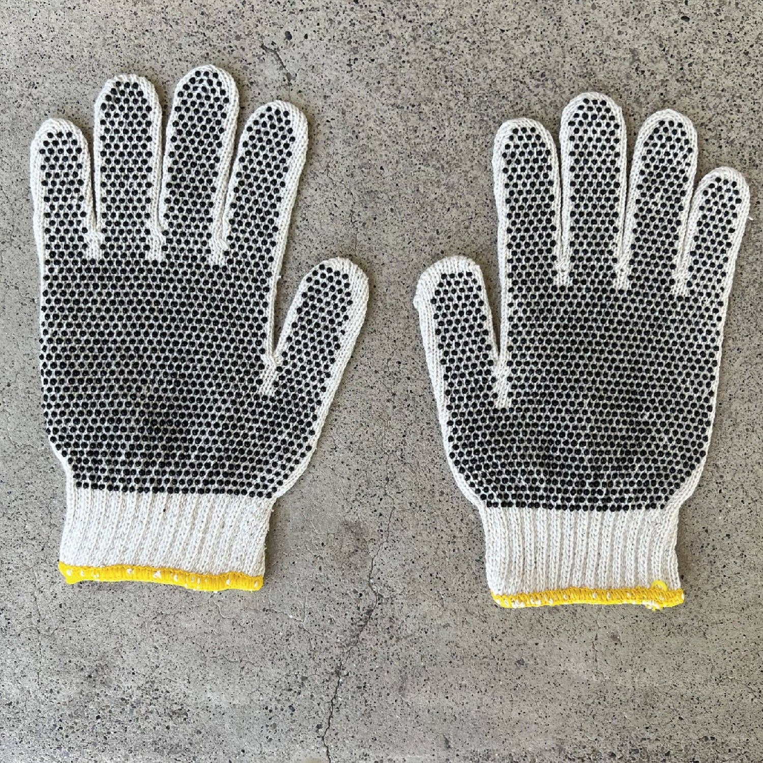 Pair of gloves with textured palm and yellow cuffs on a concrete surface
