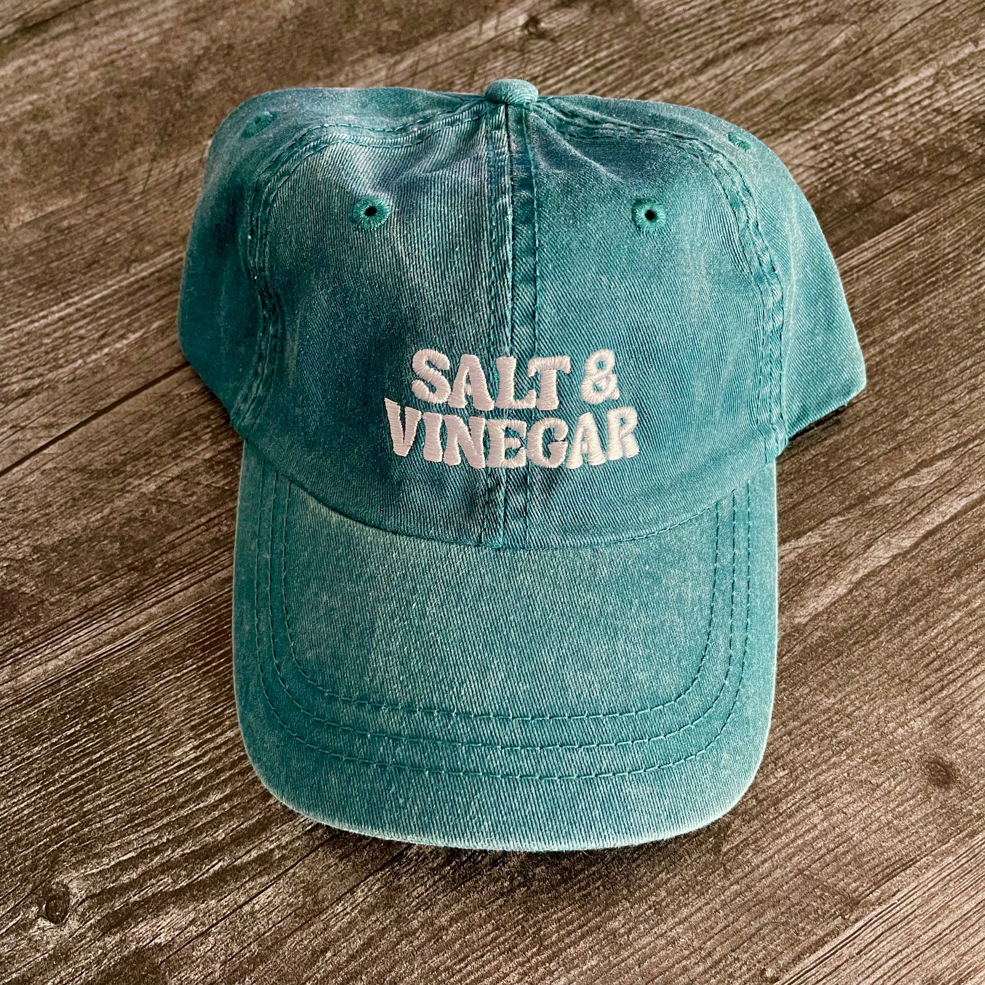 Teal cap with 'Salt & Vinegar' text on a wooden surface