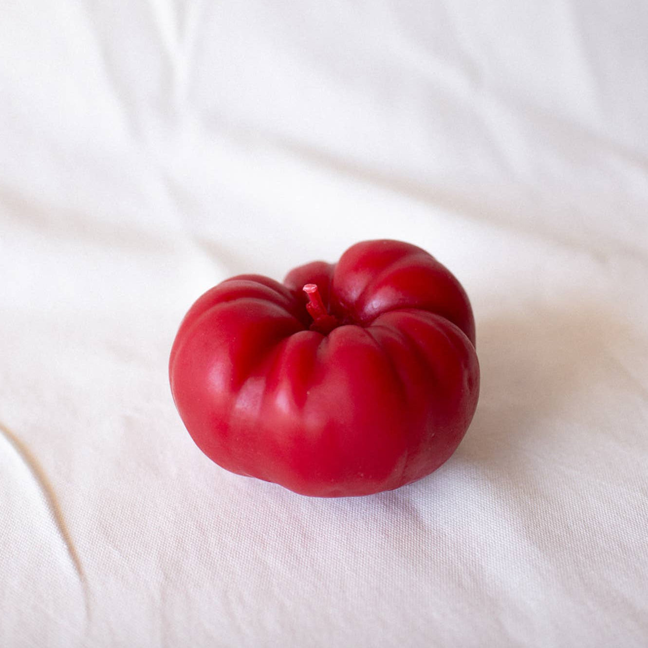 A tomato shaped beeswax candle resting on a white fabric background.