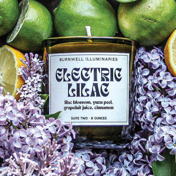 Candle labeled 'Electric Blac' surrounded by green fruits and purple flowers