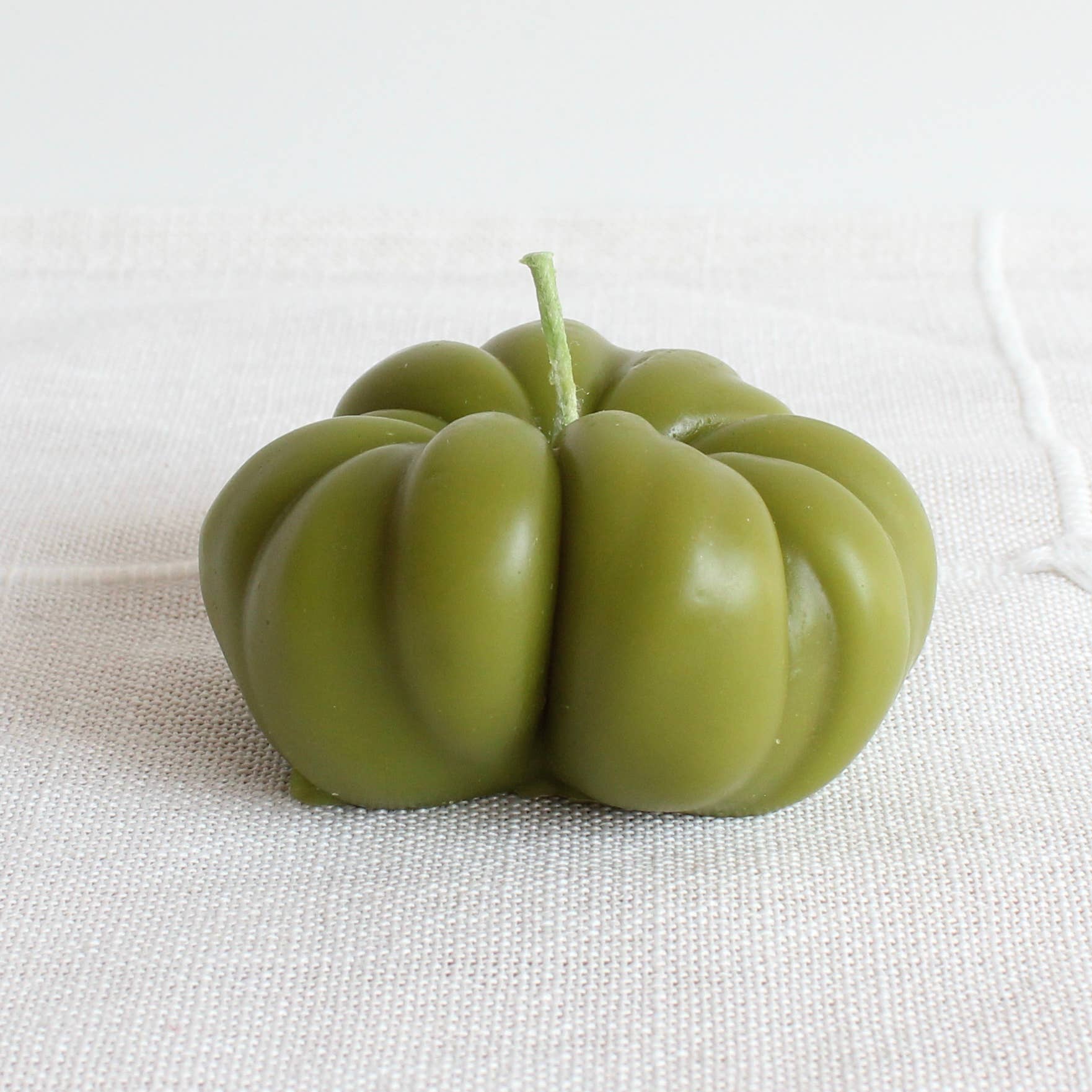 Green fruit-like candle on a textured white surface