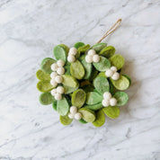 A felt mini mistletoe wreath ornament with green and white colors, featuring white beads and hanging from a string.