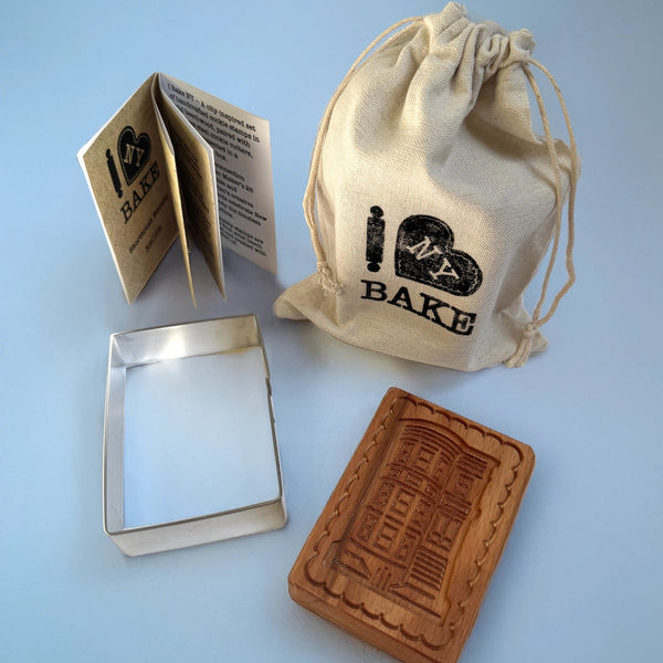 Baking set with a wooden mold, metal tray, and branded drawstring bag on a light blue background.